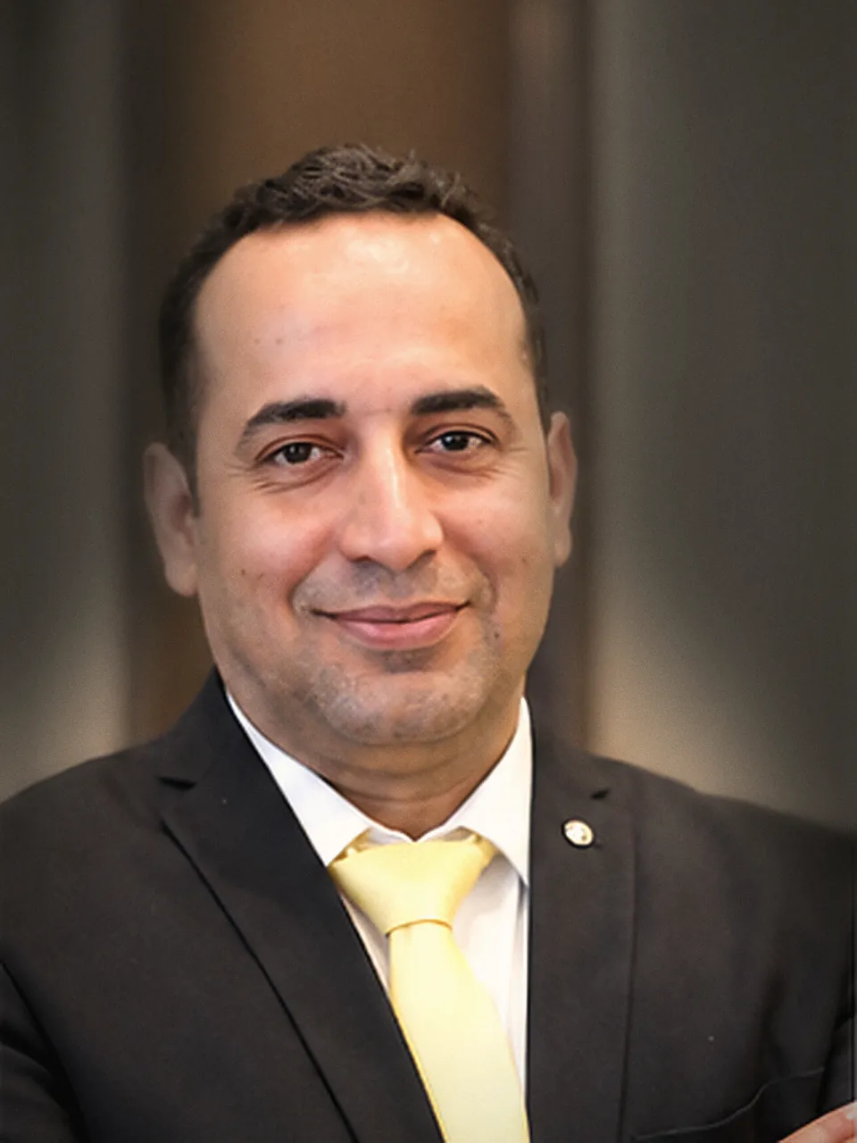Dr Ashish Mahendra in a dark suit and pale tie, arms folded, looking at the camera.