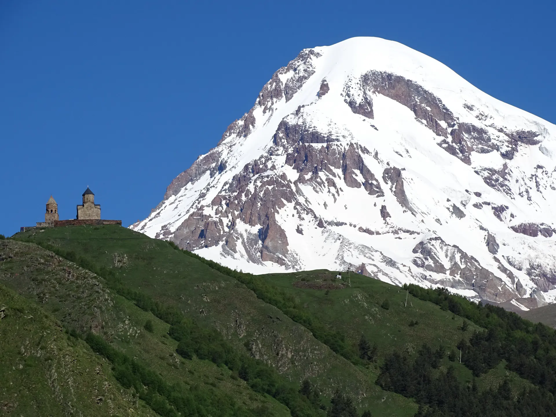 Gergeti Trinity Church on its green ridge with snow-covered Kazbek behind it.