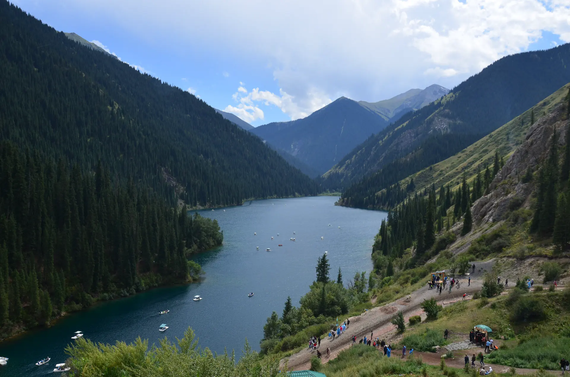 A Kolsai lake winding between forested mountains under a high sky.