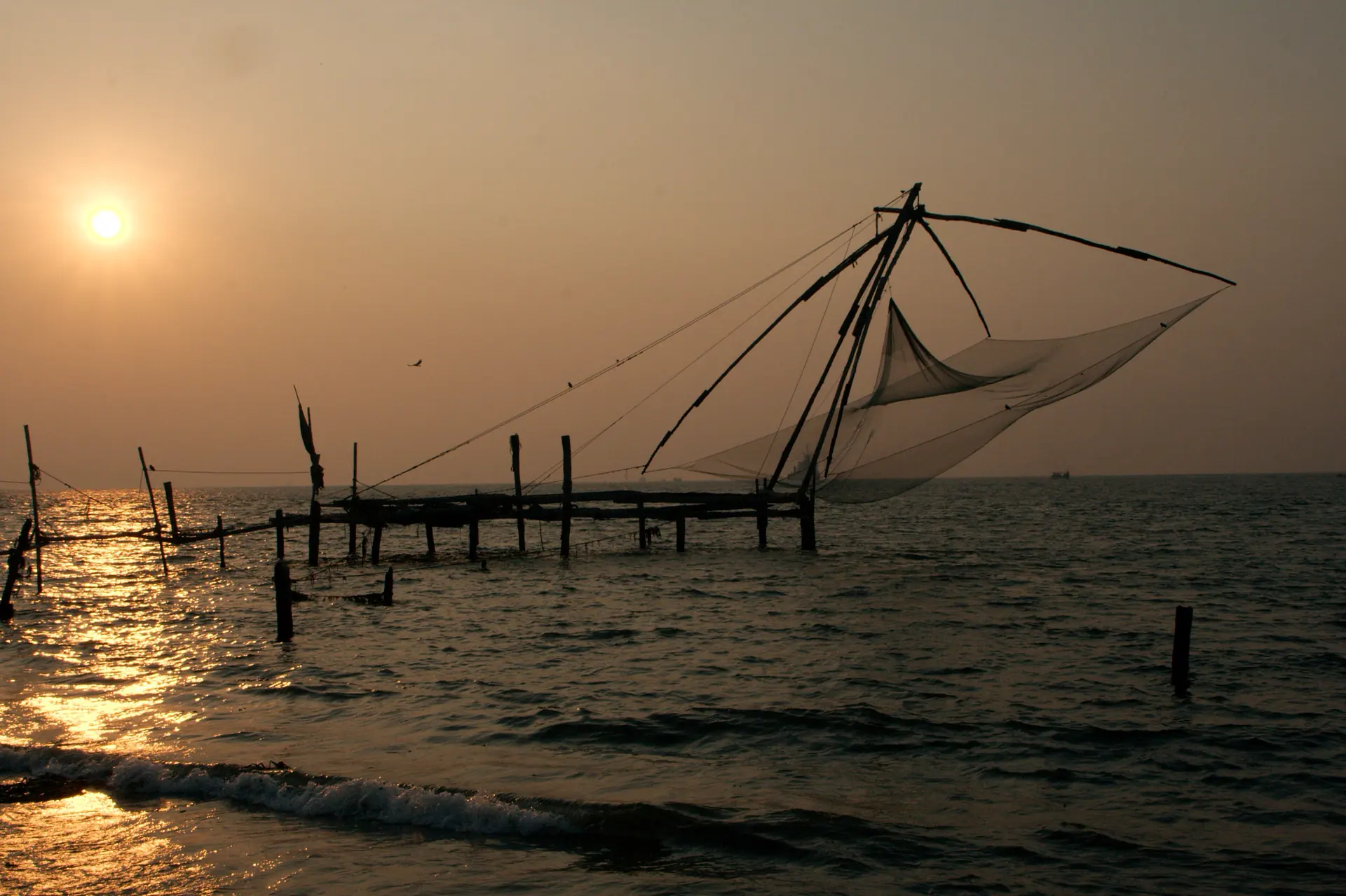 A cantilevered Chinese fishing net silhouetted against the sun at Fort Kochi.