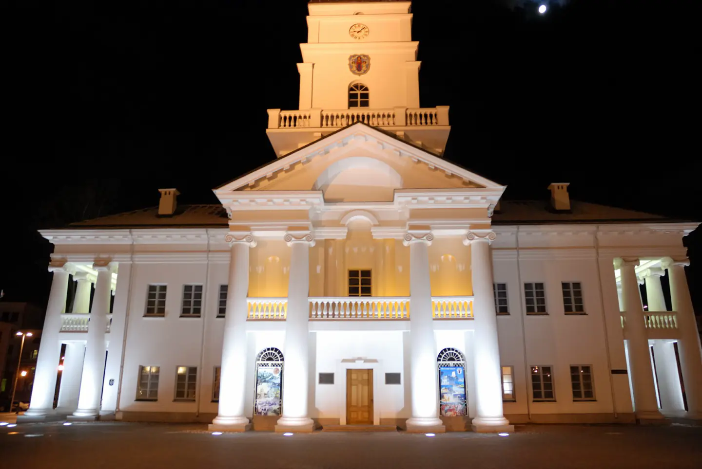 Minsk City Hall floodlit at night, its clock tower reflected on wet cobbles.