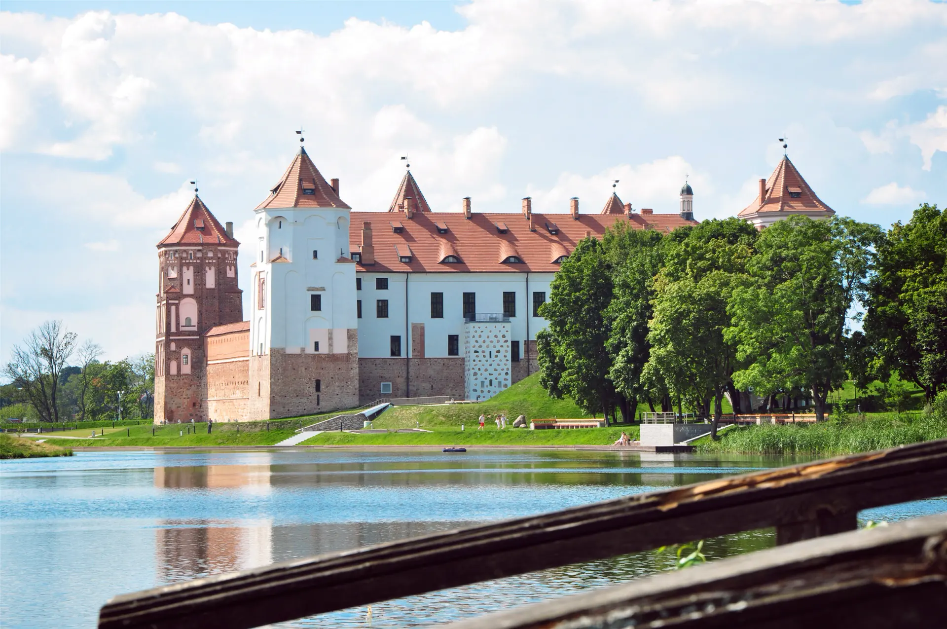 The red-brick towers of Mir Castle reflected in its lake on a still afternoon.