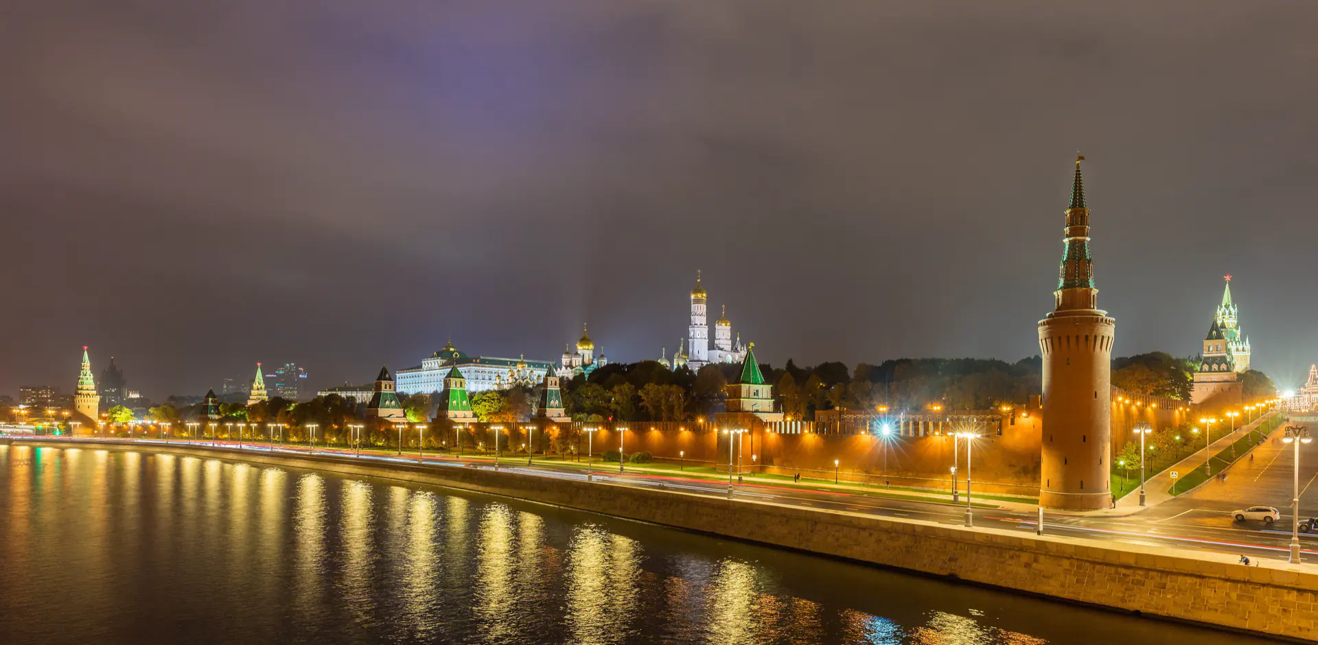 The Moscow Kremlin walls and towers along the river embankment at dusk.